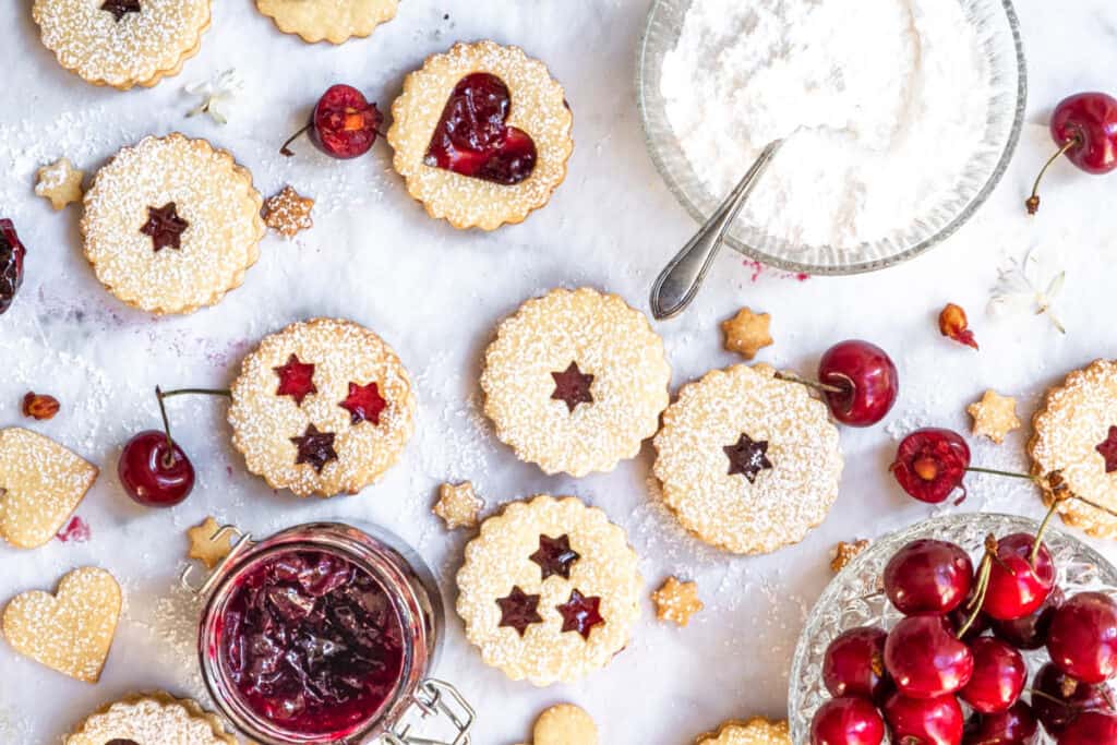 Heart Cookies with Homemade Spiced Cherry Jam shown from above next to a bowl of cherries and icing sugar 