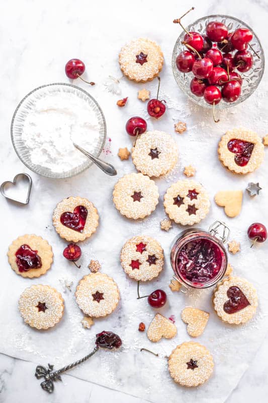 Heart Cookies with Homemade Spiced Cherry Jam shown from above on a table with cookie cutters, cherries, and icing sugar