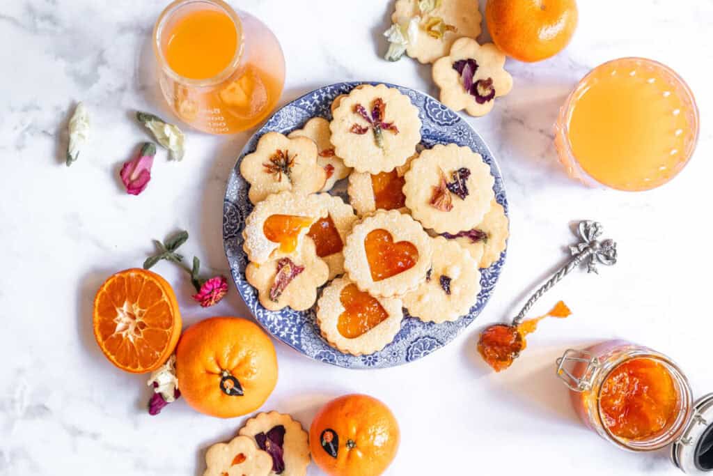 Shortbread Style Jam Sandwich Cookies shown on a plate after baking next to citrus juice. 