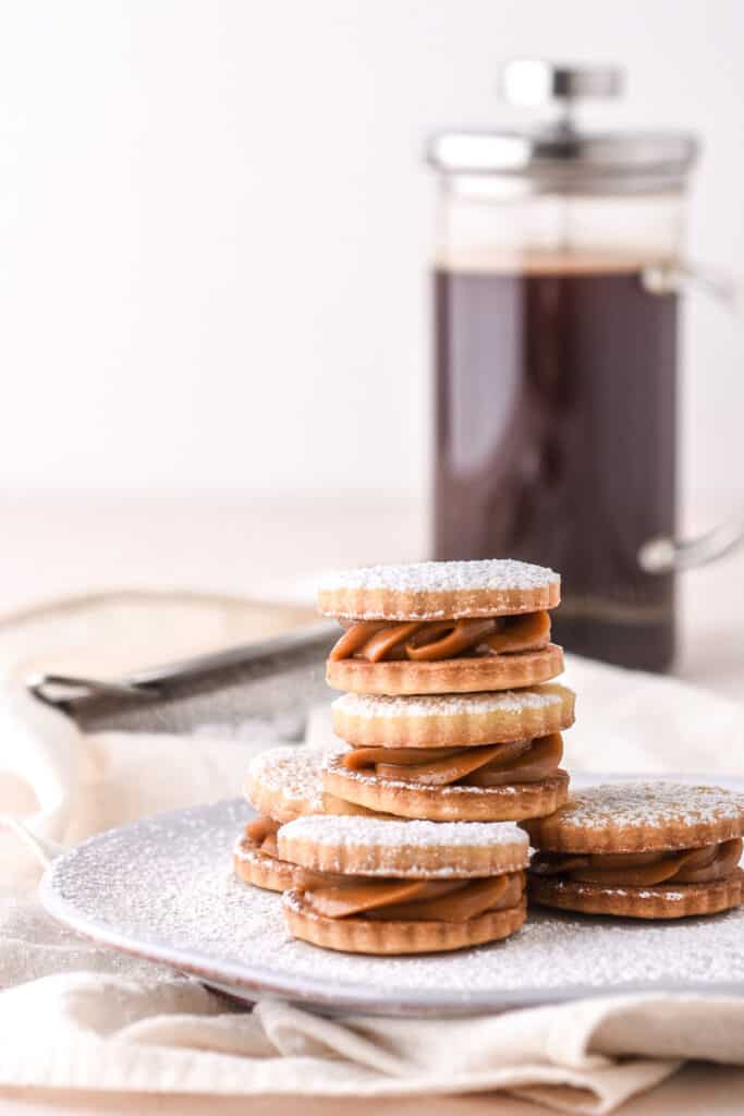 Dulce de Leche Cookies shown on a plate, with a pot of coffee in the background.