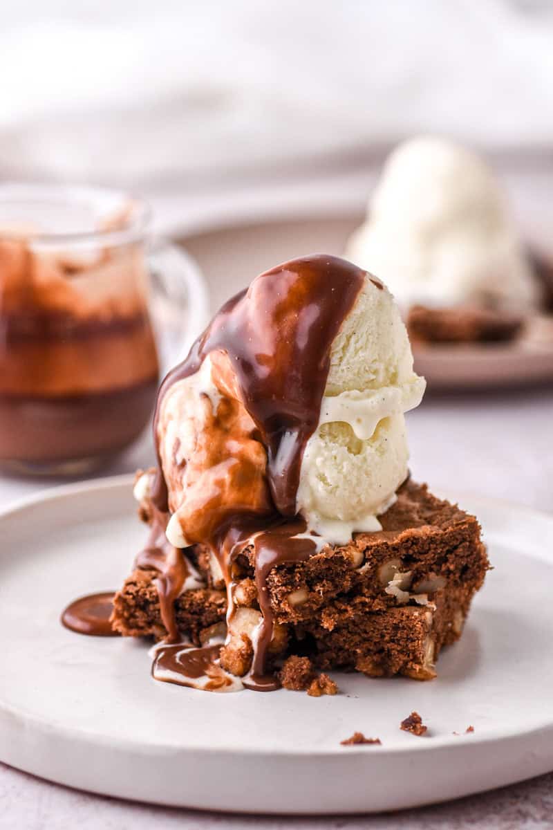 Brownies, ice cream and chocolate sauce showed stacked on a white plate. 