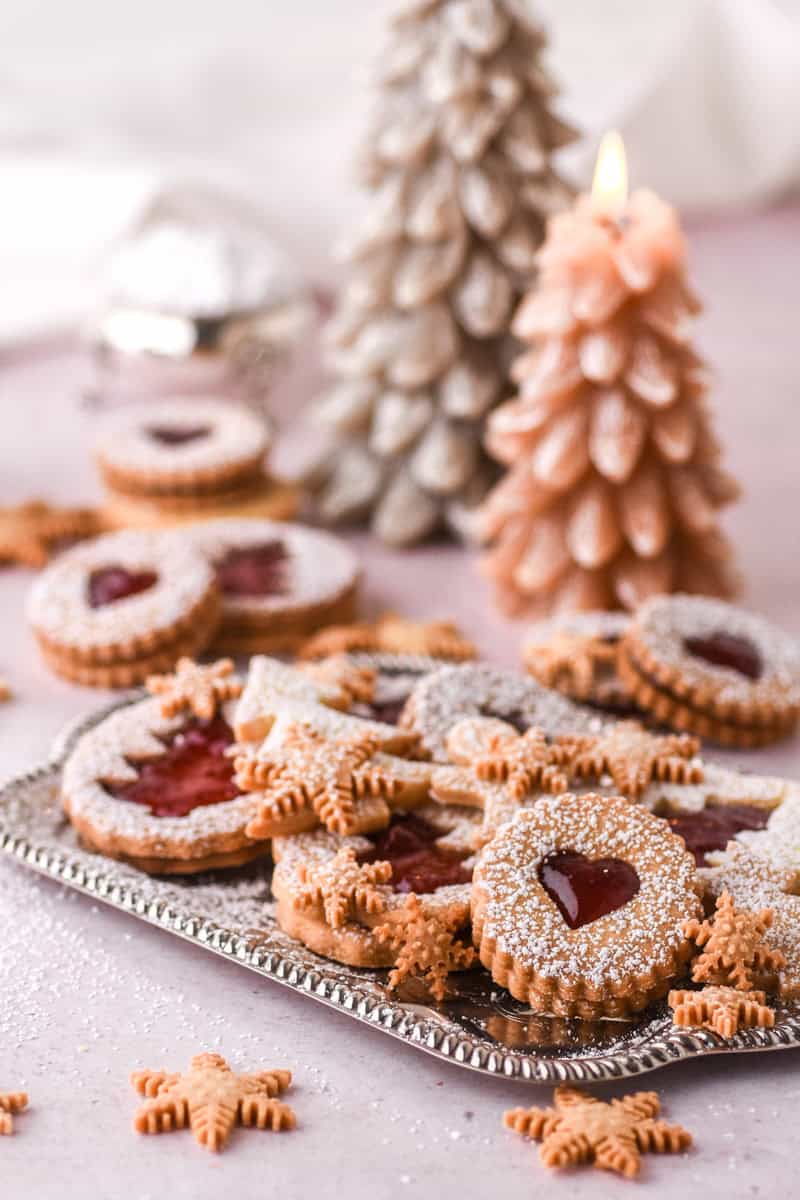 Christmas Butter Cookies of different shapes shown on a silver tray there are Christmas tree candles in the background.