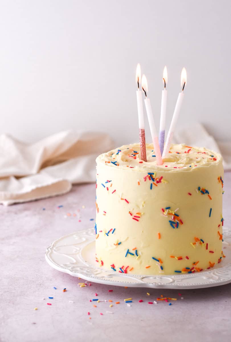 Image shows the cake on a white plate with different coloured candles in the cake that have been lit. 