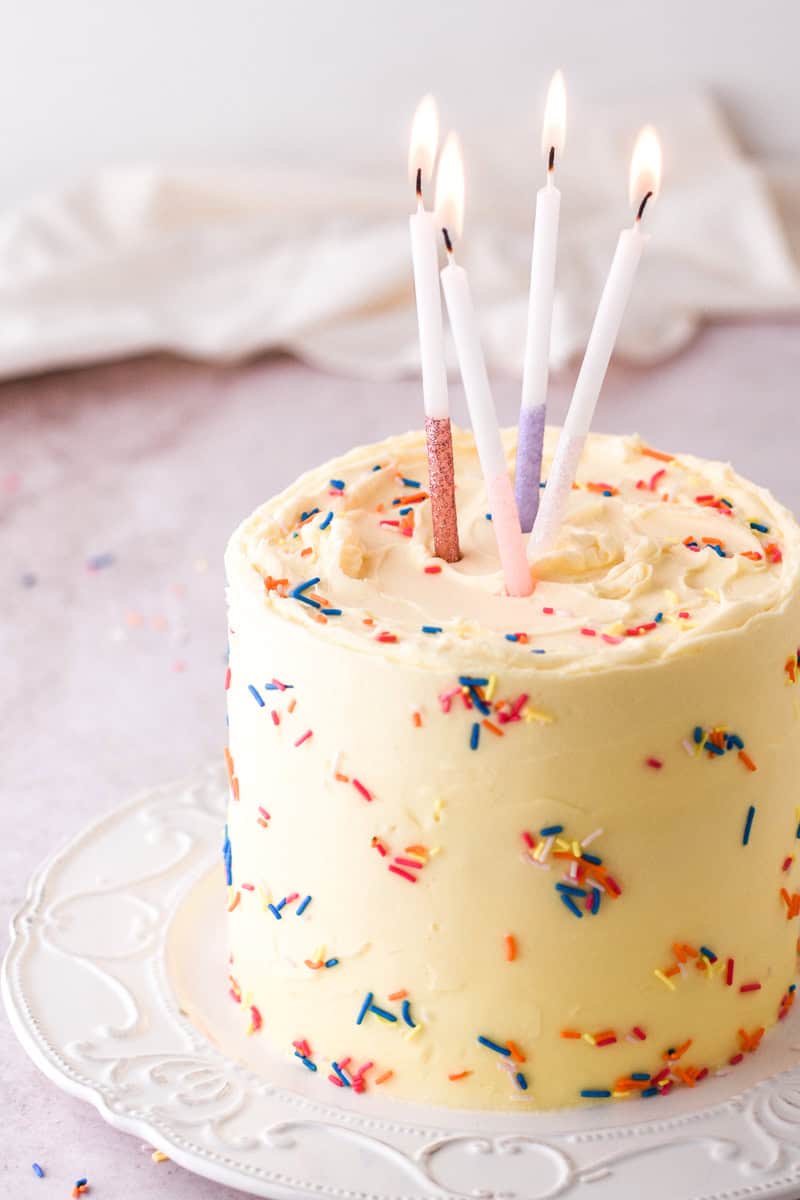 Image shows the final decorated cake on a plate with different coloured glitter candles sticking out of the cake. 