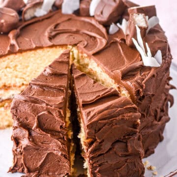 Bounty cake shown sliced on a cake plate, you can see the vanilla cake covered in chocolate frosting.