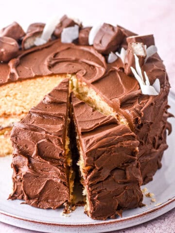 Bounty cake shown sliced on a cake plate, you can see the vanilla cake covered in chocolate frosting.