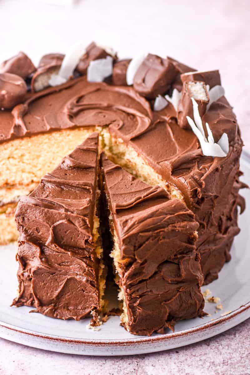 Image showing the cake on a cake plate, a few slices have been cut so you can see the contrast between the chocolate frosting and vanilla cake. 