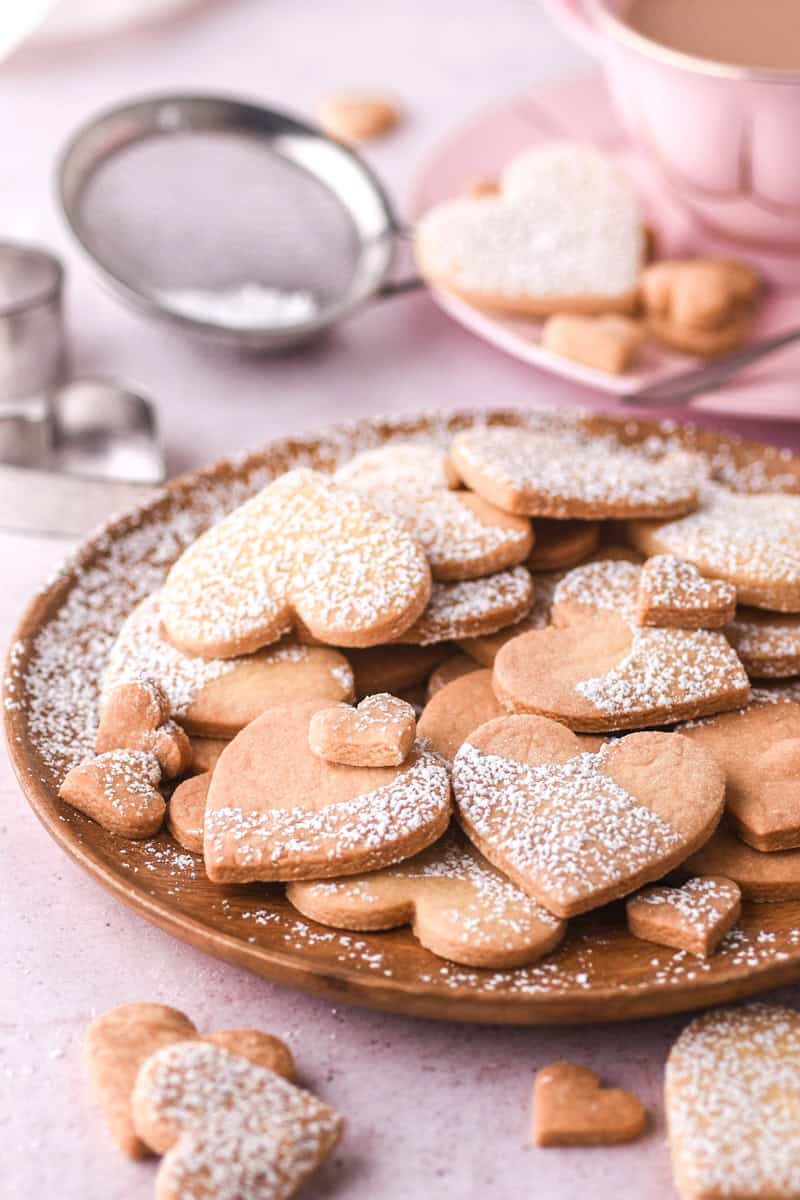 Heart shaped cookies dusted with icing sugar shown on a wooden plate. 