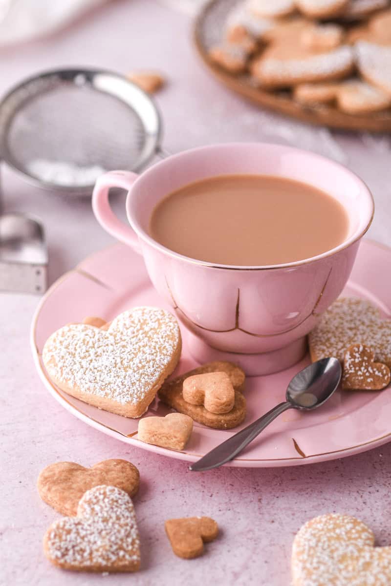 Heart cookies shown on a pink saucer next to a cup of milk tea.