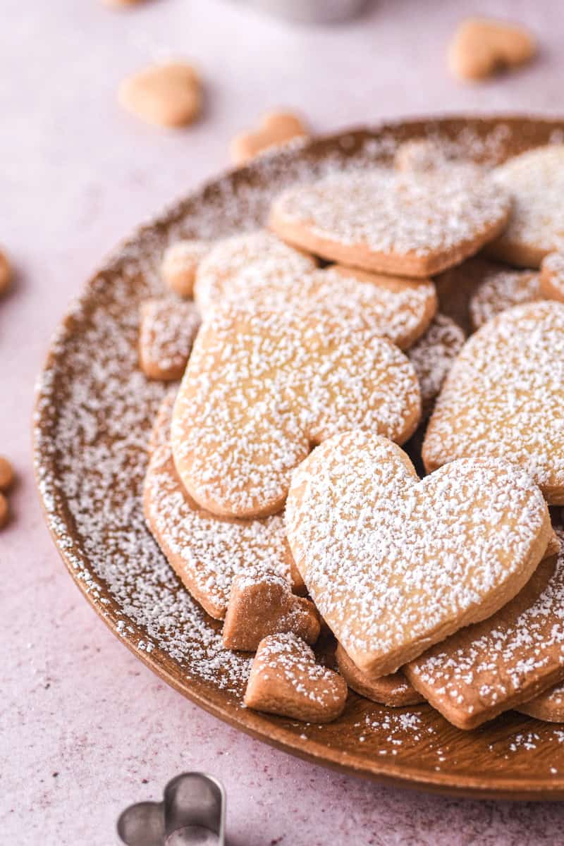 Different sized heart cookies dusted with icing sugar shown on a plate. 