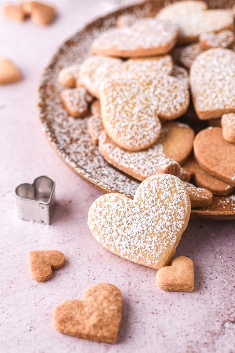 Heart Shaped Biscuits shown on a wooden plate, one cookie is off the plate and shown close up. 